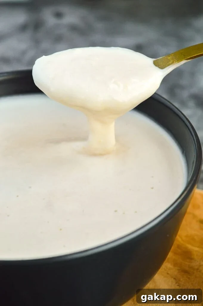 Close-up of a gold spoon dipping into a bowl of white creamy sauce