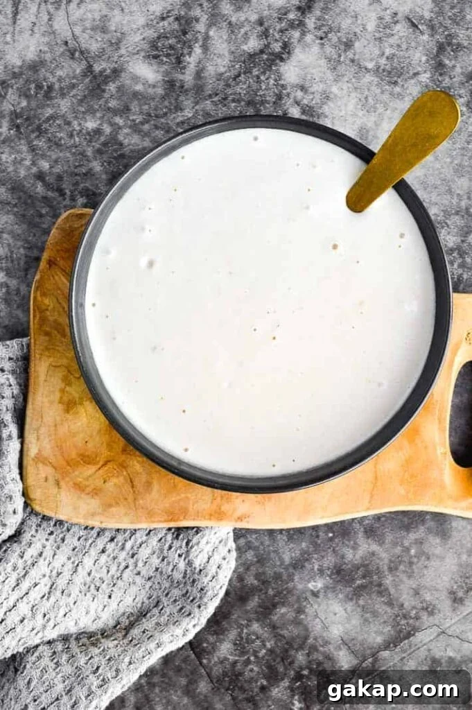 A black bowl on a wooden board on a grey background with thick white sauce in it