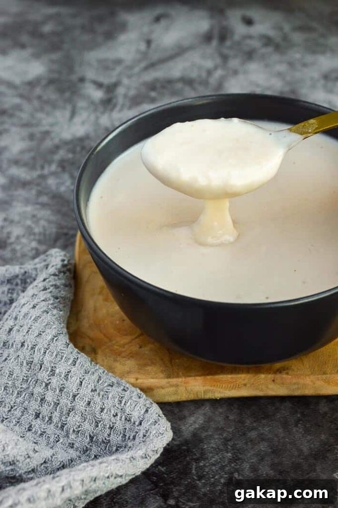 A spoon with thick white sauce dropping off it into a black bowl