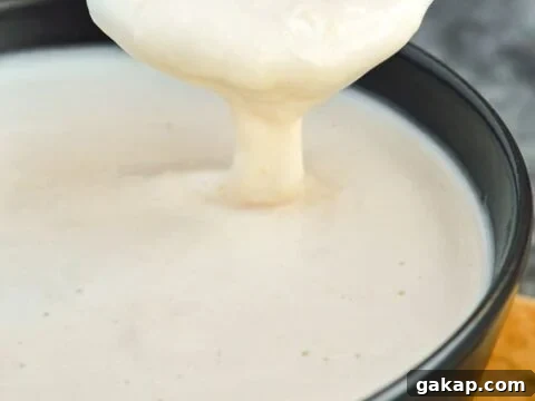 Close-up of a gold spoon dipping into a bowl of white creamy sauce
