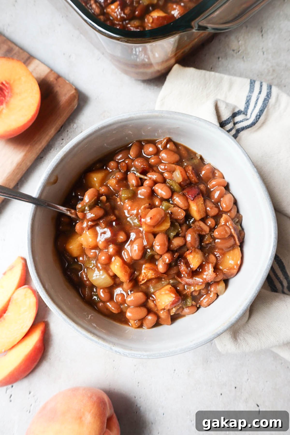 Chipotle Peach Baked Beans Recipe for Sweet-Spicy BBQ Sides 2 white bowl with peach baked beans surrounded by fresh peaches.