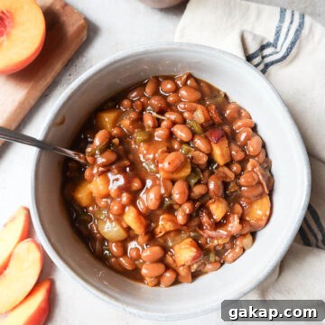 Chipotle Peach Baked Beans Recipe for Sweet-Spicy BBQ Sides 13 white bowl with peach baked beans surrounded by fresh peaches.