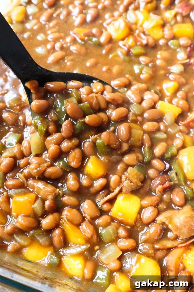 Chipotle Peach Baked Beans Recipe for Sweet-Spicy BBQ Sides 8 glass baking dish with spoon scooping peach baked beans.