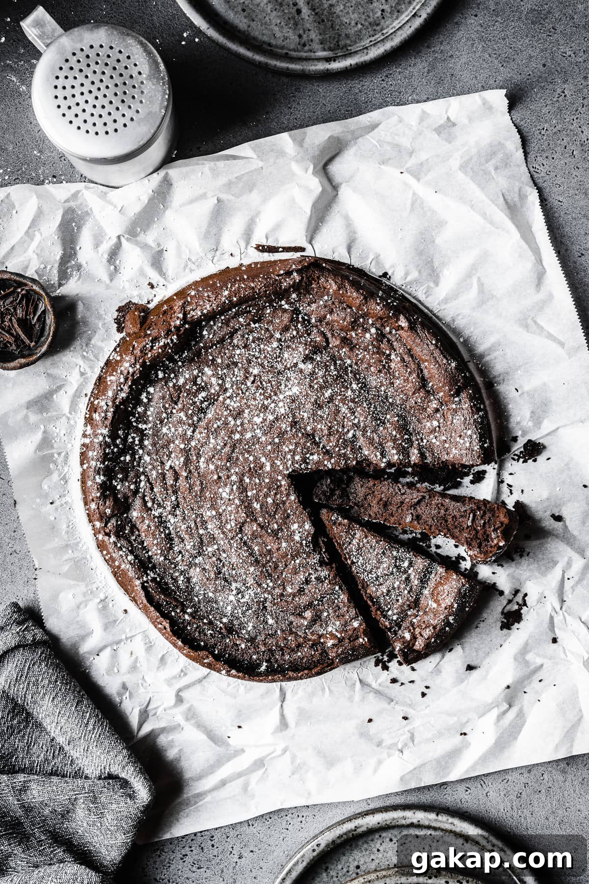 A dense single layer chocolate cake on parchment paper with two slices cut.