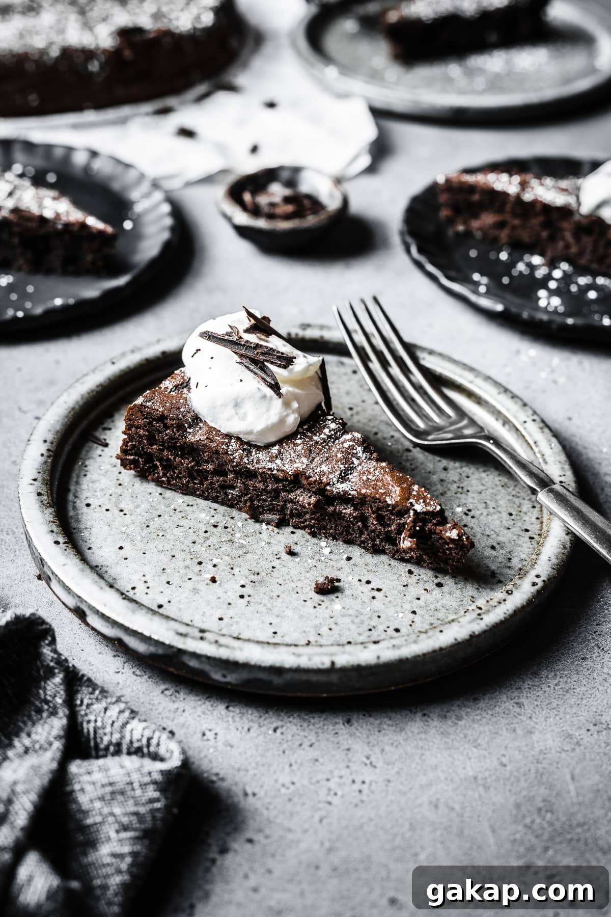 A slice of dense chocolate cake topped with whipped cream and chocolate shavings.