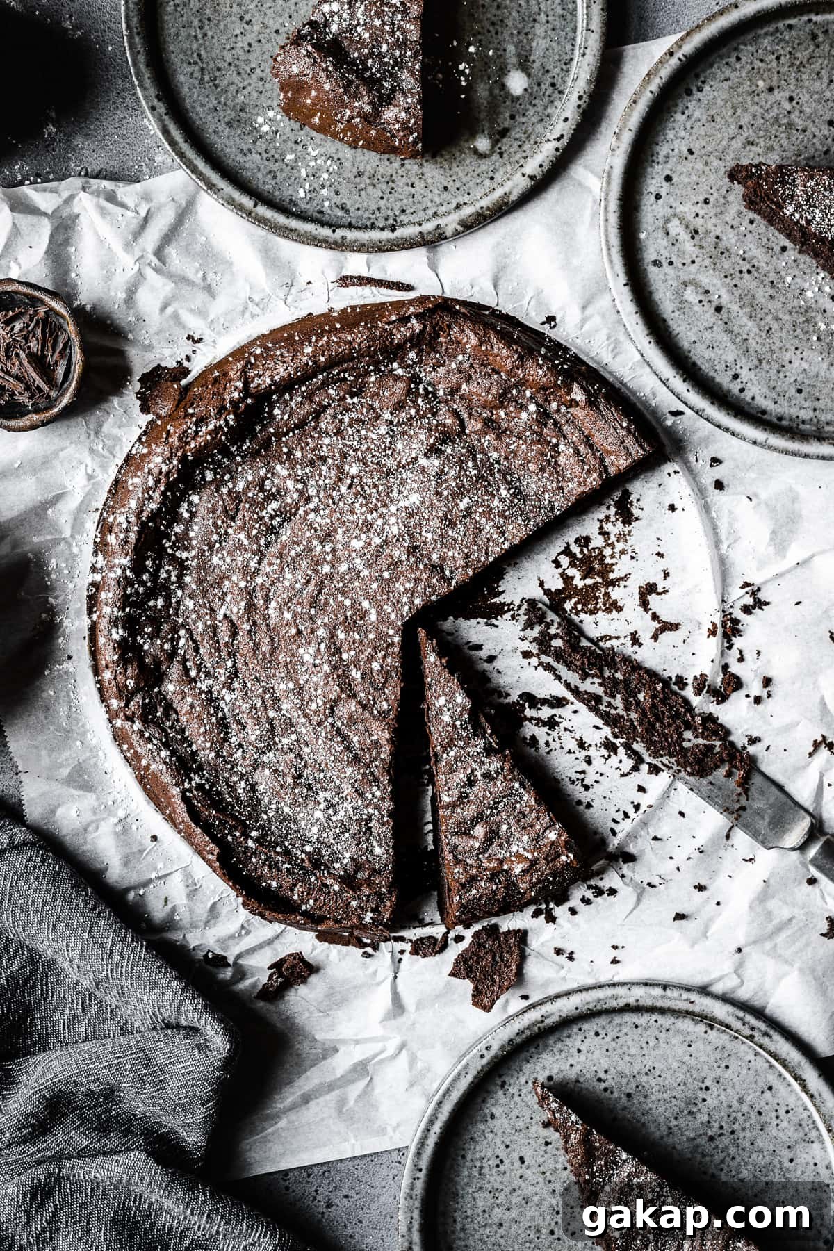 A dark chocolate torta tenerina with slices cut out on grey plates.
