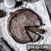 A single layer chocolate cake sprinkled with powdered sugar on white parchment paper.