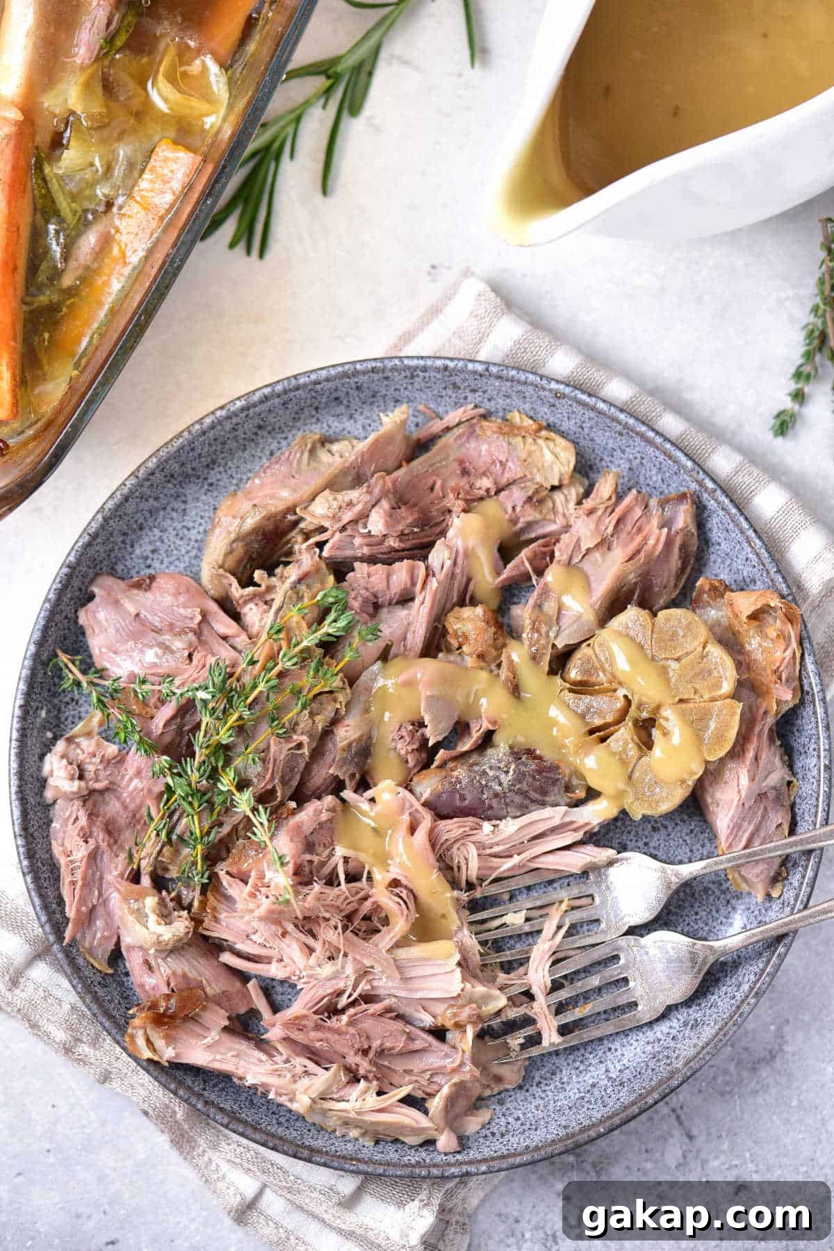 Perfect Slow-Roasted Leg of Lamb Recipe for Tender Meat 2 Grey plate with serving of roasted lamb. Silver forks. White surface with gravy boat.