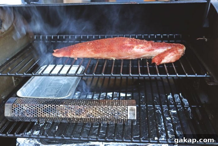pork tenderloin being smoked on pellet grill with tube smoker lit underneath