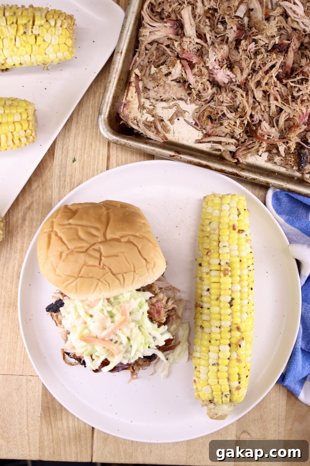Smoky Pulled Pork is so simple to make on the grill. pulled pork on a tray and plated on a sandwich with coleslaw served with corn on the cob
