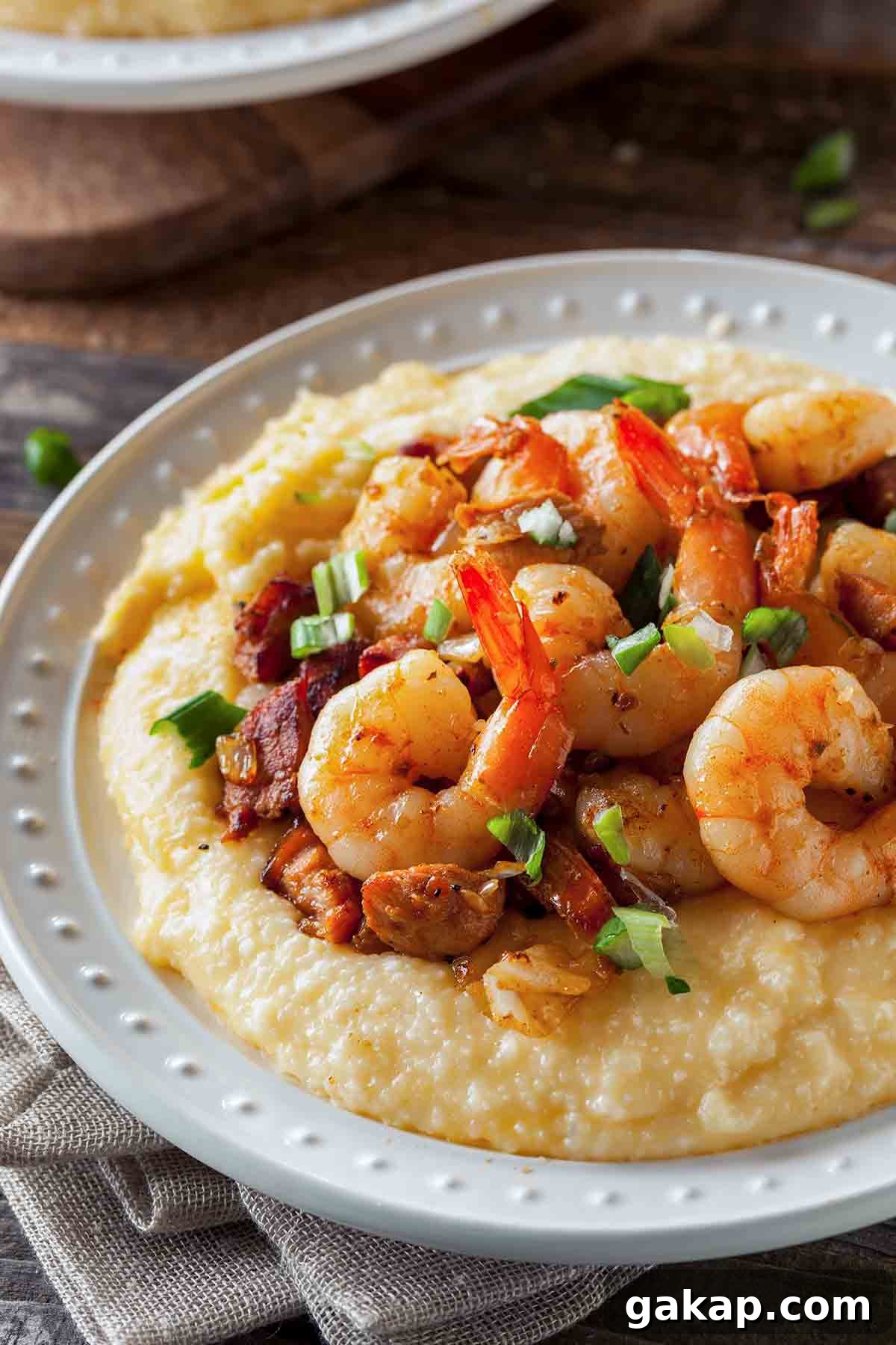 A white plate filled with cheesy shrimp and grits with bacon
