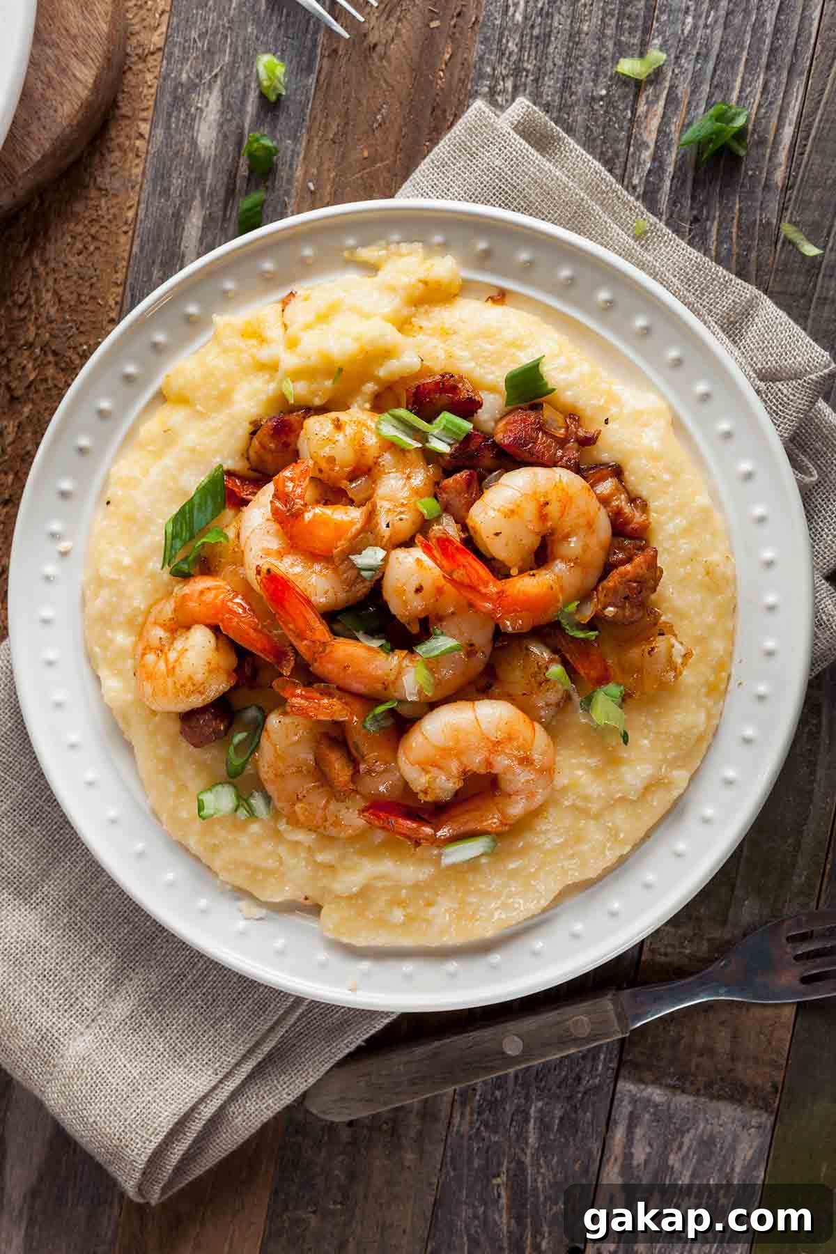 A white plate filled with cheesy shrimp and grits with bacon