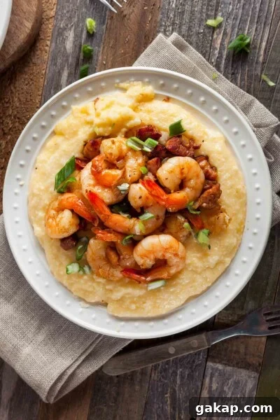 A white plate filled with cheesy shrimp and grits with bacon