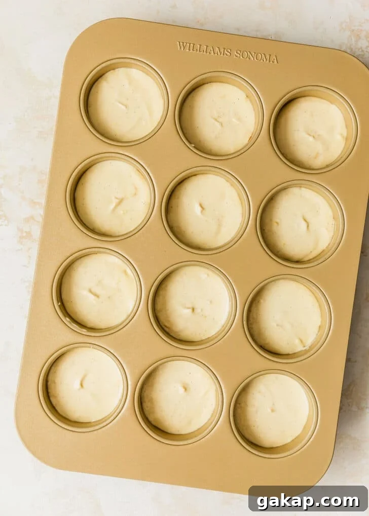 A gold pan of raw mini creme brulee cheesecakes on a tan counter.