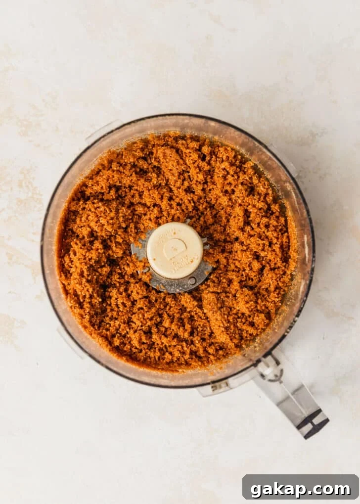 A food processor of graham cracker crust on a beige table.