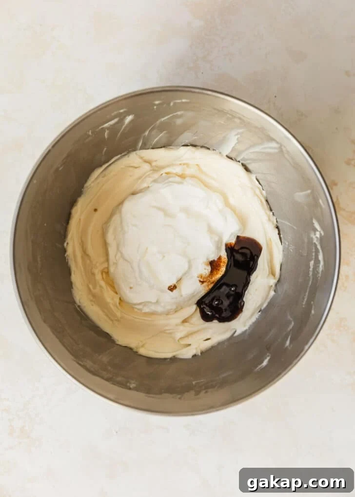 A silver bowl of cream cheese, sour cream, and vanilla bean paste on a beige table.