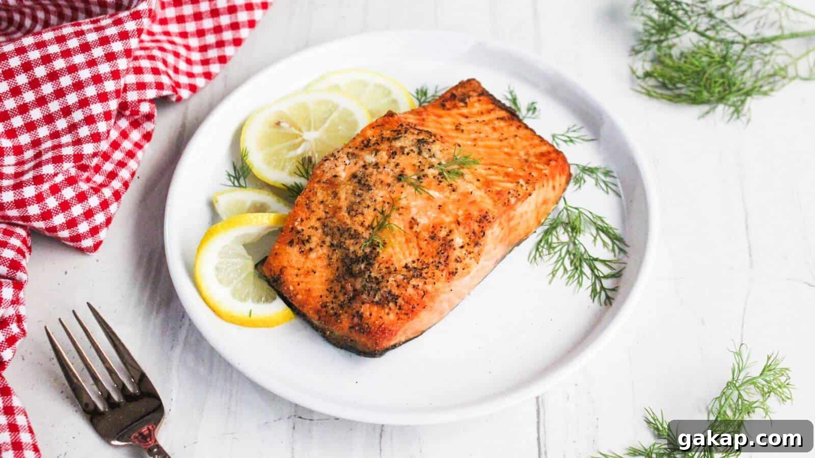 Grilled salmon fillet on a white plate garnished with lemon slices and dill, next to a red checkered cloth and a fork.