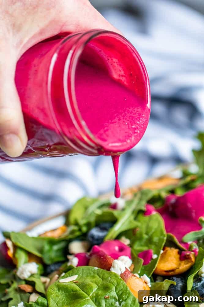 Hand pouring blueberry dressing over a salad.