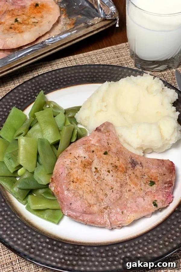 Tender oven baked Pork Chop with a bone on a plate with green beans and mashed potatoes.