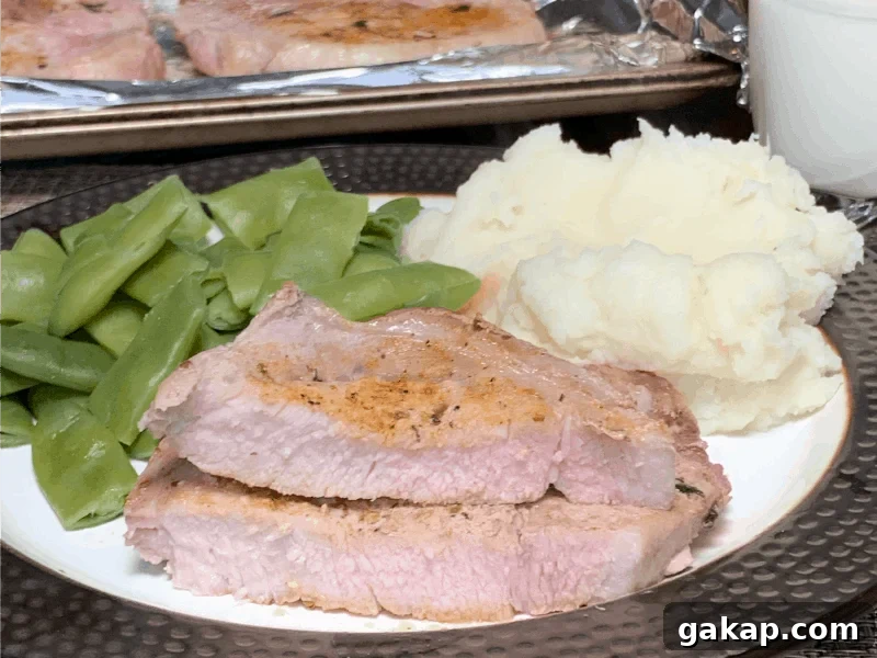 bone in pork chop sliced in half to reveal juicy center cooked to 145F with green beans and mashed potatoes on a large plate