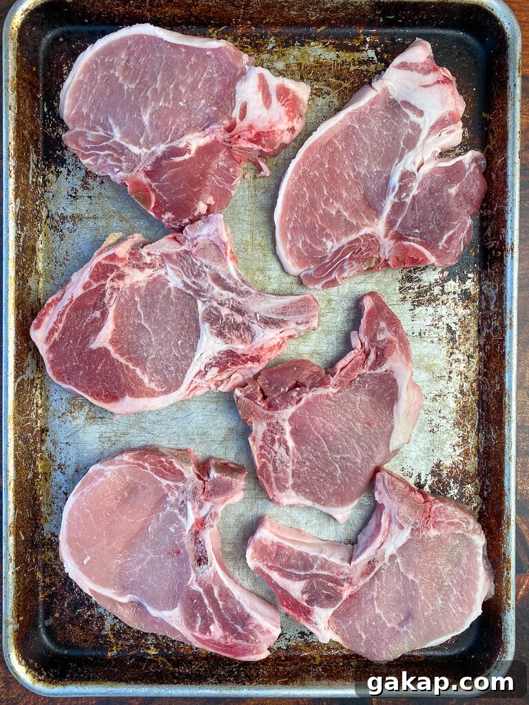 Pink bone-in pork chops on a silver baking sheet sitting to knock the chill off