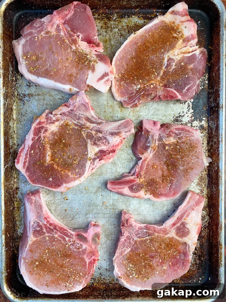 Six bone-in pork loin center cut chops rubbed with seasoning on a large baking sheet