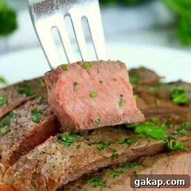 A fork holds a slice of medium-rare steak garnished with chopped herbs.