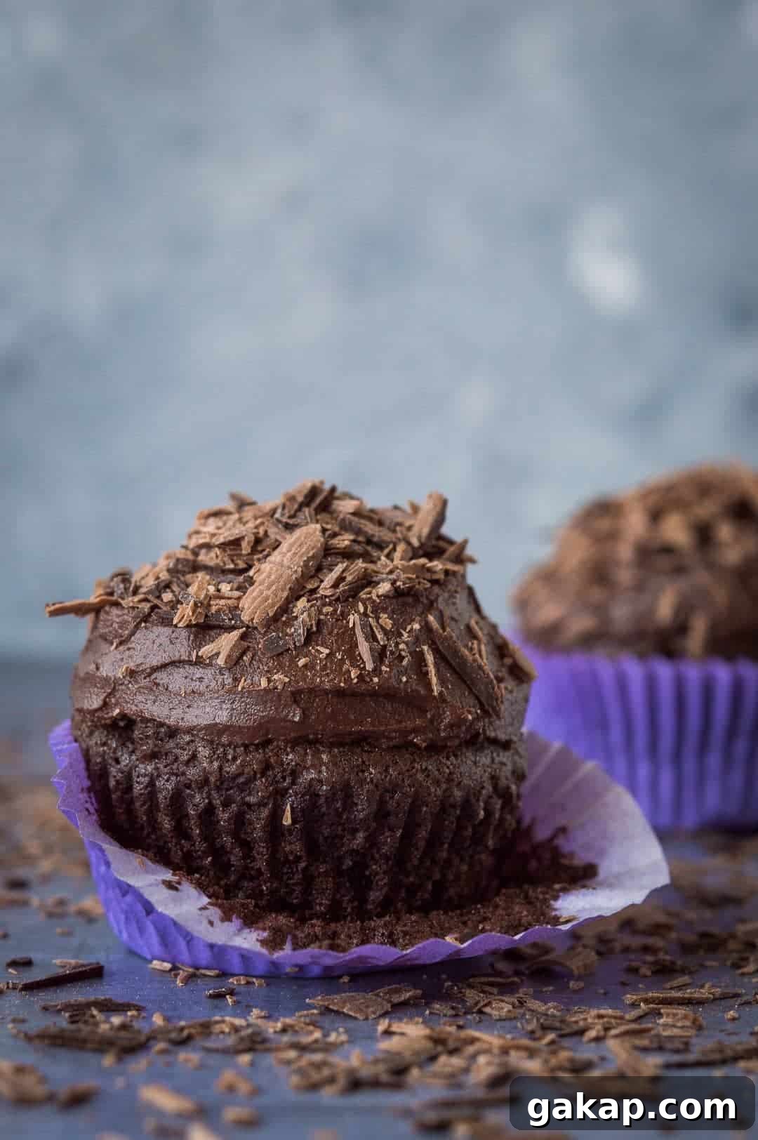 Chocolate cupcakes for two - a small batch of just two delicious vegan chocolate cupcakes that are incredibly quick and easy to whip up and so tasty! Perfect for Valentines Day. #vegan #veganbaking #vegancupcakes #smallbatch close up of a chocolate cupcake topped with buttercream and chocolate shavings with the wrapper peeled down.