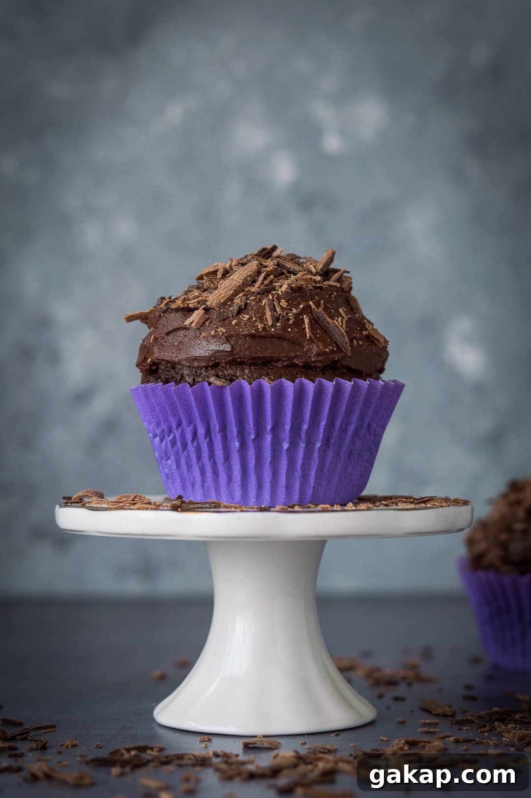Chocolate cupcakes for two - a small batch of just two delicious vegan chocolate cupcakes that are incredibly quick and easy to whip up and so tasty! Perfect for Valentines Day. #vegan #veganbaking #vegancupcakes #smallbatch A vegan chocolate cupcake on top of a mini cake stand scattered with chocolate shavings.