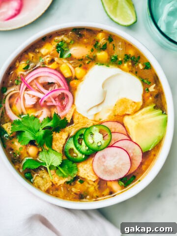 Vegan Green Chili Soup in a bowl with sour cream, pickled onions and cilantro.