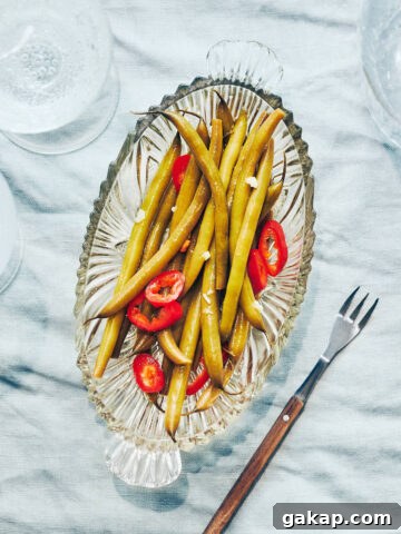 Plate of pickled green beans and peppers on a table with sparkling water on the side