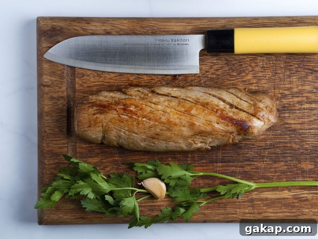 seared pork tenderloin on a wooden cutting board with fresh herbs