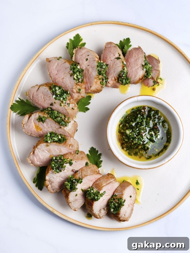 sous vide pork tenderloin sliced on a white platter with green herb sauce