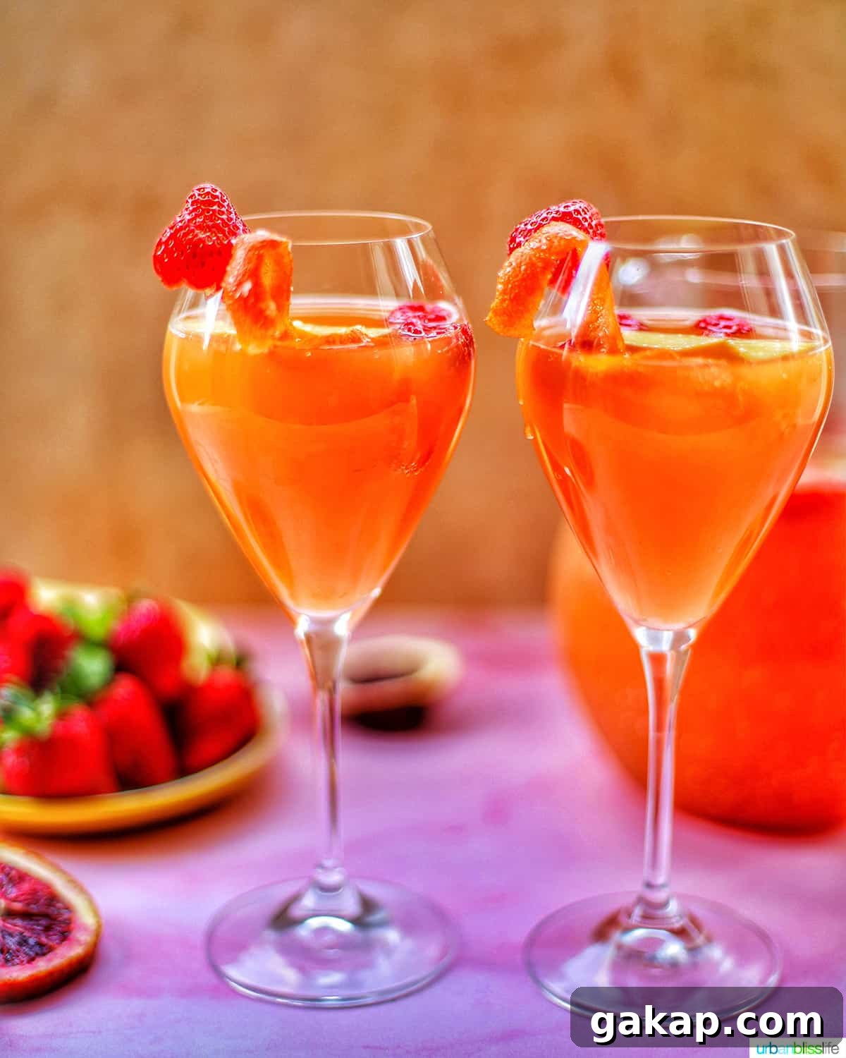 two glasses of tropical sangria with raspberries and citrus on a pink table with berries and a pitcher of sangria in the background.
