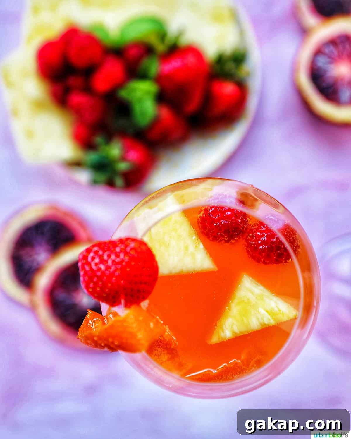 glass of tropical sangria with fruit slices in the drink on a pink background with fruit on a plate in the background.
