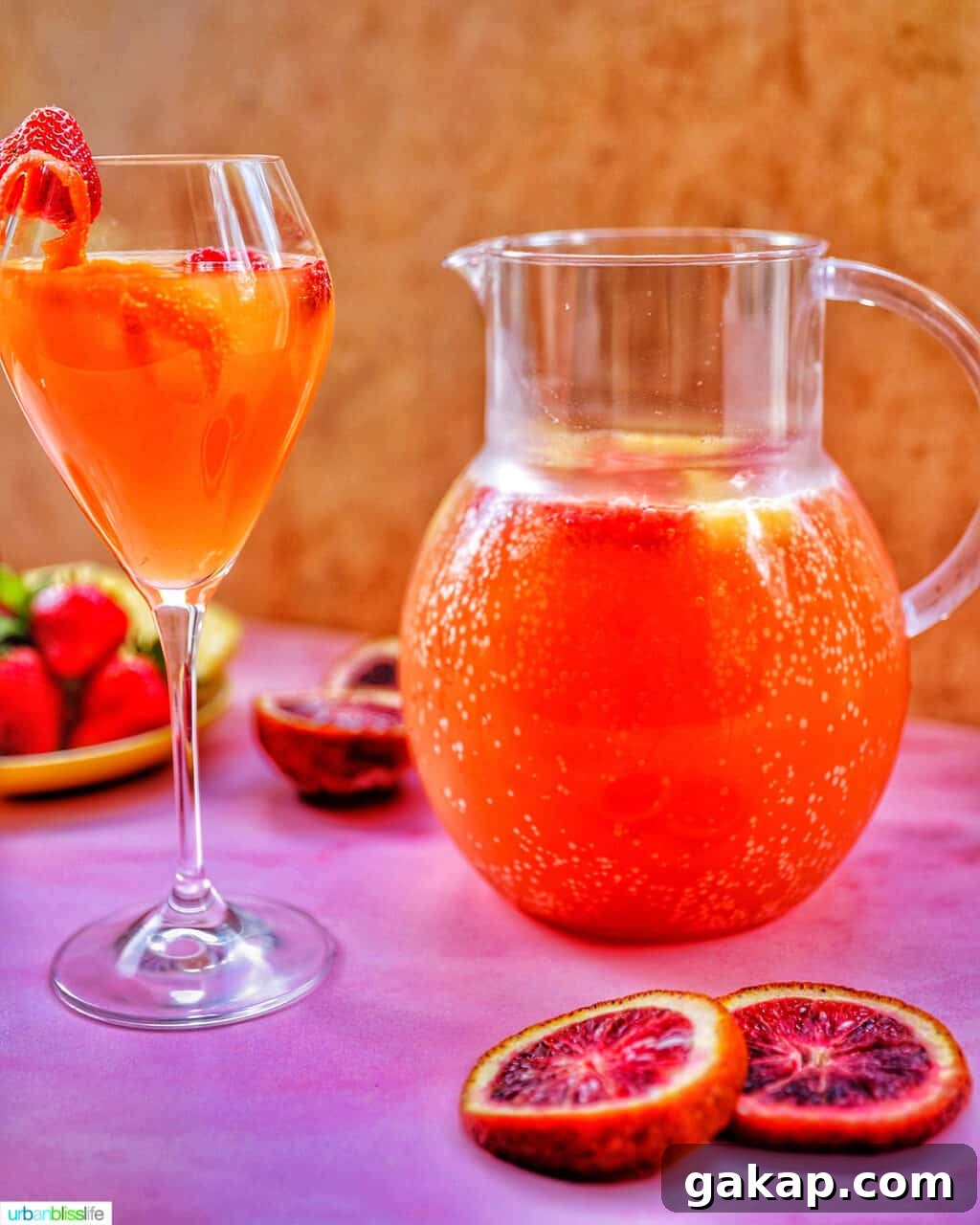 glass of tropical sangria with raspberries and citrus on a pink table with berries and a pitcher of sangria in the background.