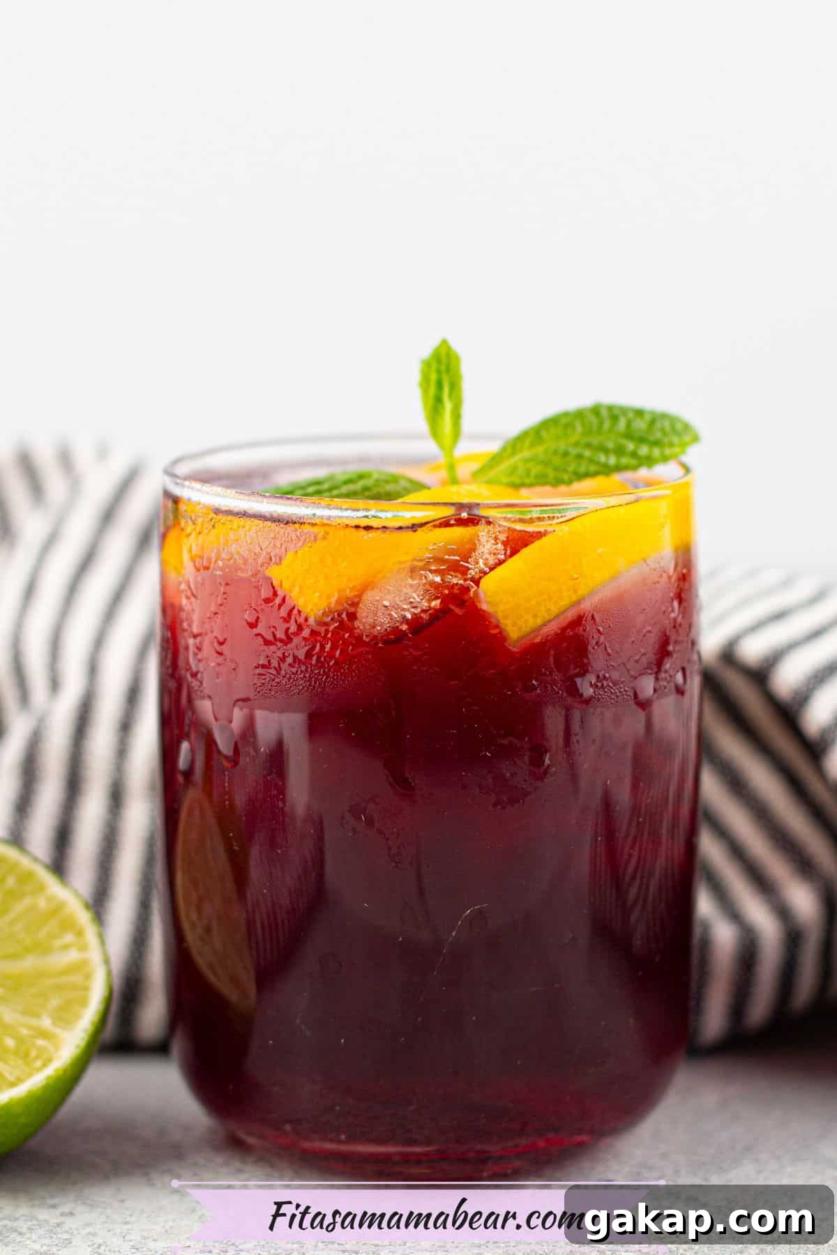 Sparkling Kombucha Mocktail Recipe for Refreshing Summer Sips 2 Red kombucha mocktail in a glass garnished with mint leaves and orange slices.