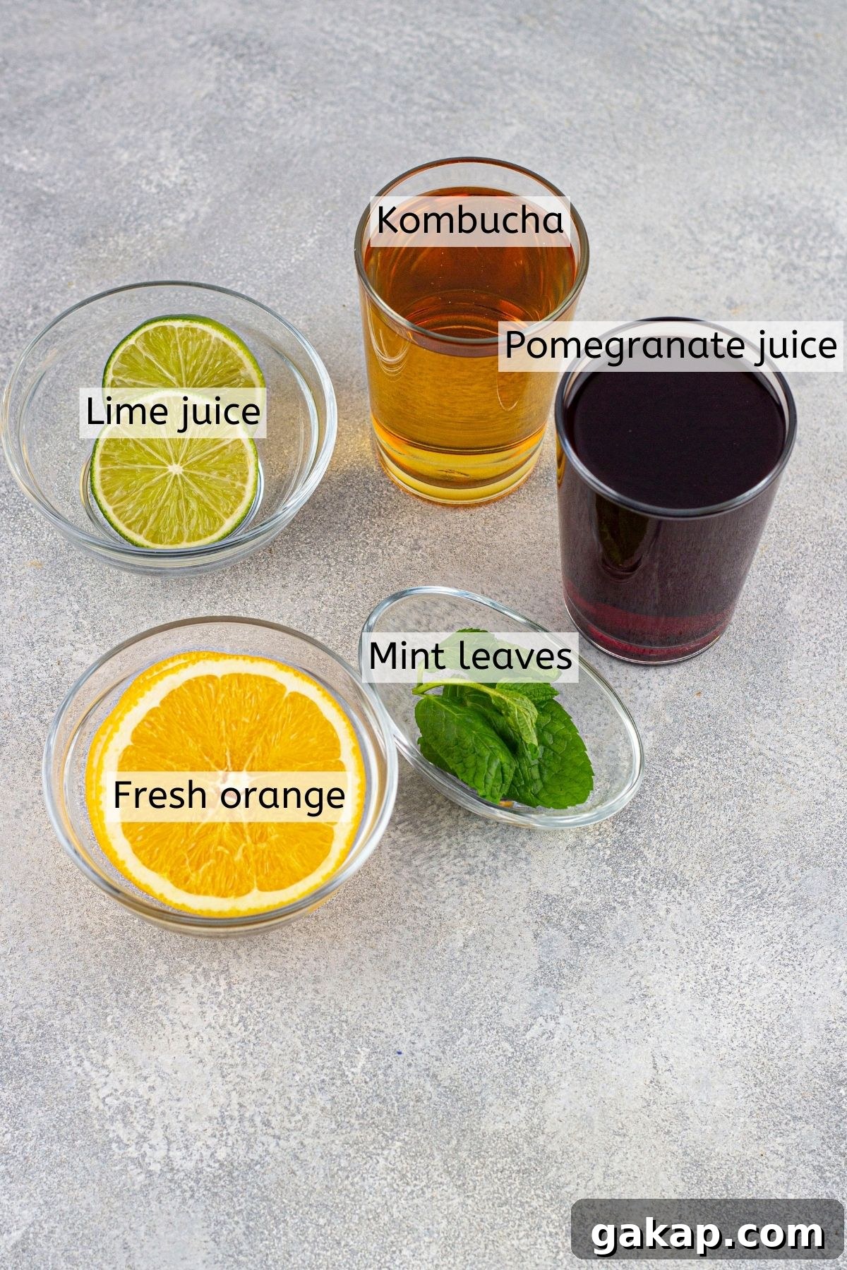 Sparkling Kombucha Mocktail Recipe for Refreshing Summer Sips 3 Kombucha, juice, oranges, limes, and mint leaves in glass containers with text labels over top of them.
