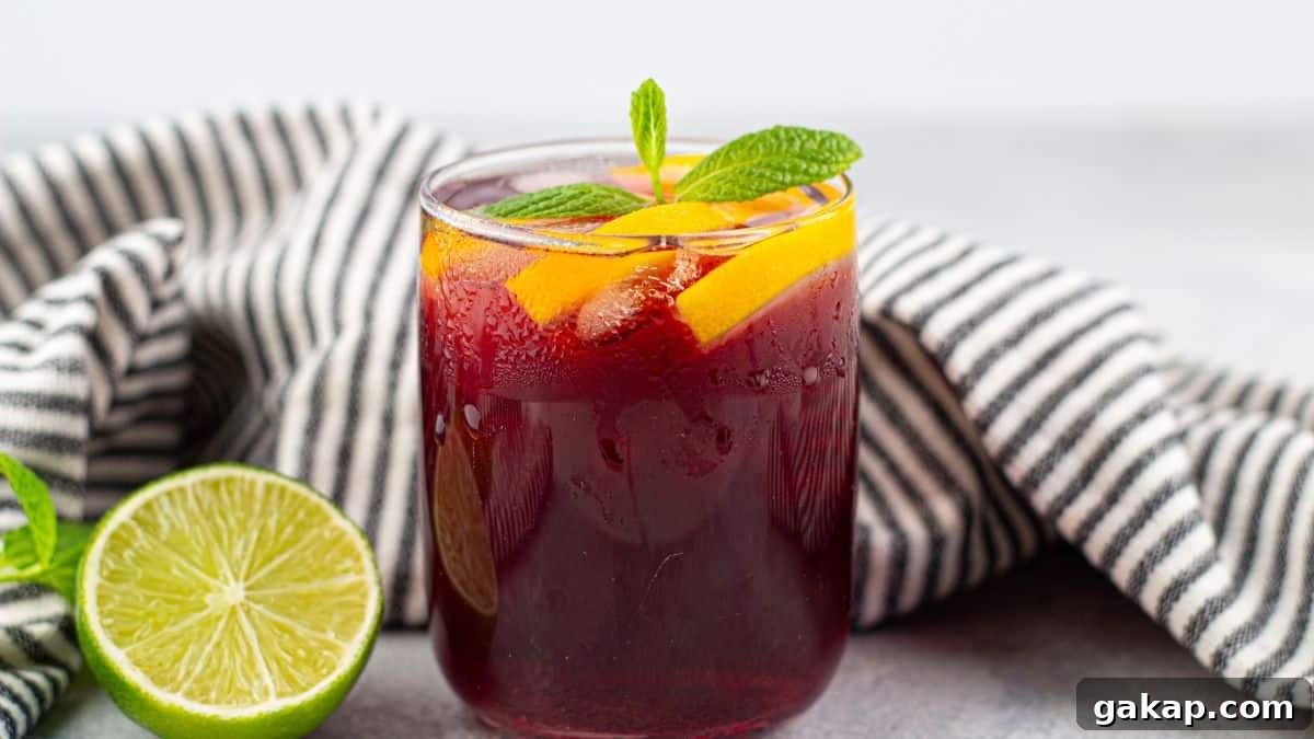 Sparkling Kombucha Mocktail Recipe for Refreshing Summer Sips 7 Red kombucha mocktail in a glass garnished with mint leaves and orange slices.