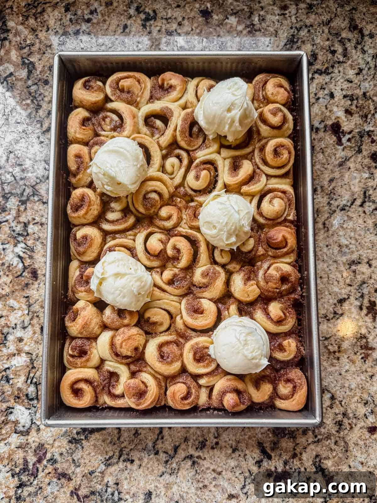 warm mini cinnamon rolls in a 9x13 pan with scoops of cream cheese frosting on top.