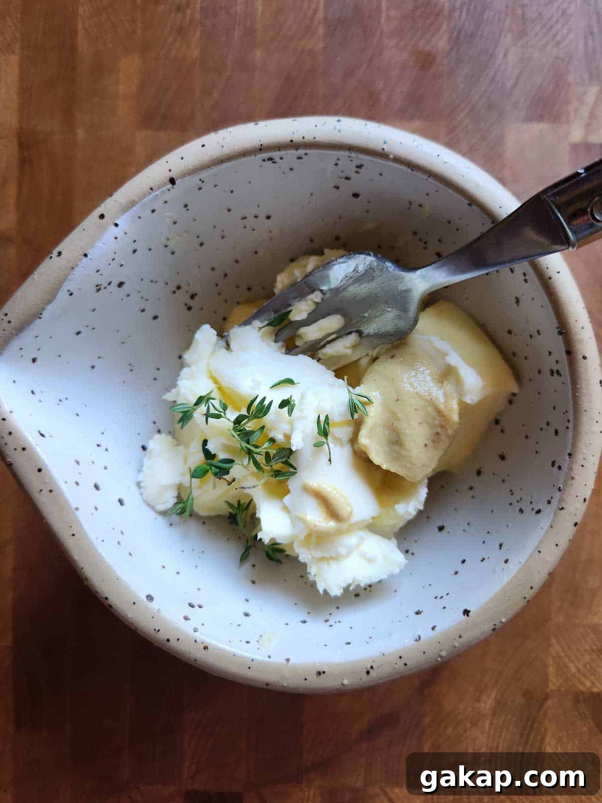 Butter, herbs and seasoning in a beige bowl with with a fork.