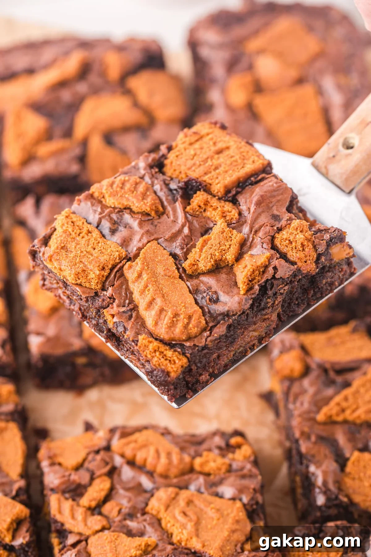 A brownie on a spatula, covered with Lotus Biscoff biscuit pieces.