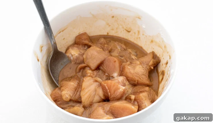 marinating cubed chicken with soy sauce and cornstarch in white bowl