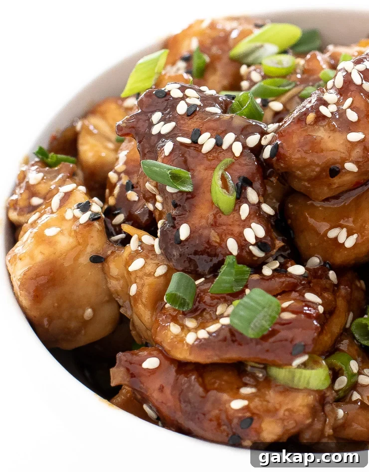 cubed asian chicken in white bowl topped with sesame seeds and green onions