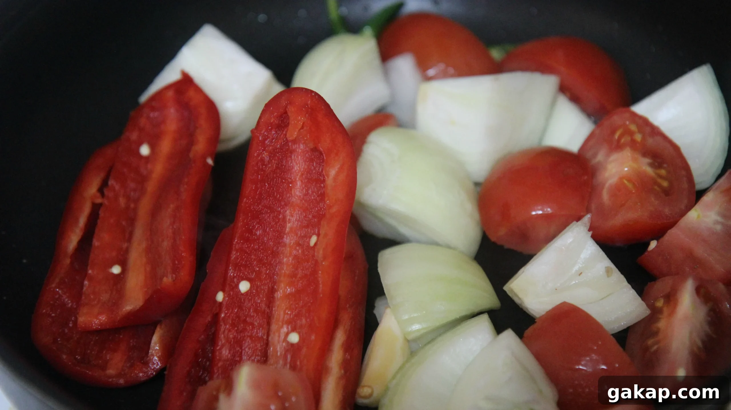 raw peppers, onions, and tomatoes in a black skillet.