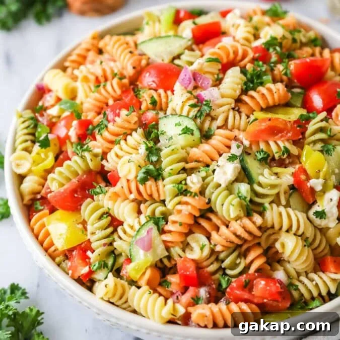 Bowl of pasta salad made with tri-color rotini, veggies, and feta cheese.