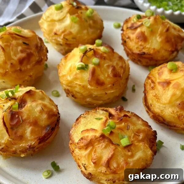 Crispy Hasselback Potatoes with Garlic Butter and Parmesan 4 A plate of golden-brown Individual Dauphinoise Potatoes stacked neatly and garnished with chopped green onions. The stacks are crispy on the edges and beautifully arranged on a white plate.