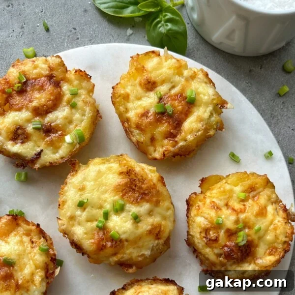 Crispy Hasselback Potatoes with Garlic Butter and Parmesan 7 Six golden-brown baked egg muffins topped with chopped green herbs are arranged on a white round serving board, next to a sprig of basil and a bowl of cheesy smashed potatoes on a gray surface.