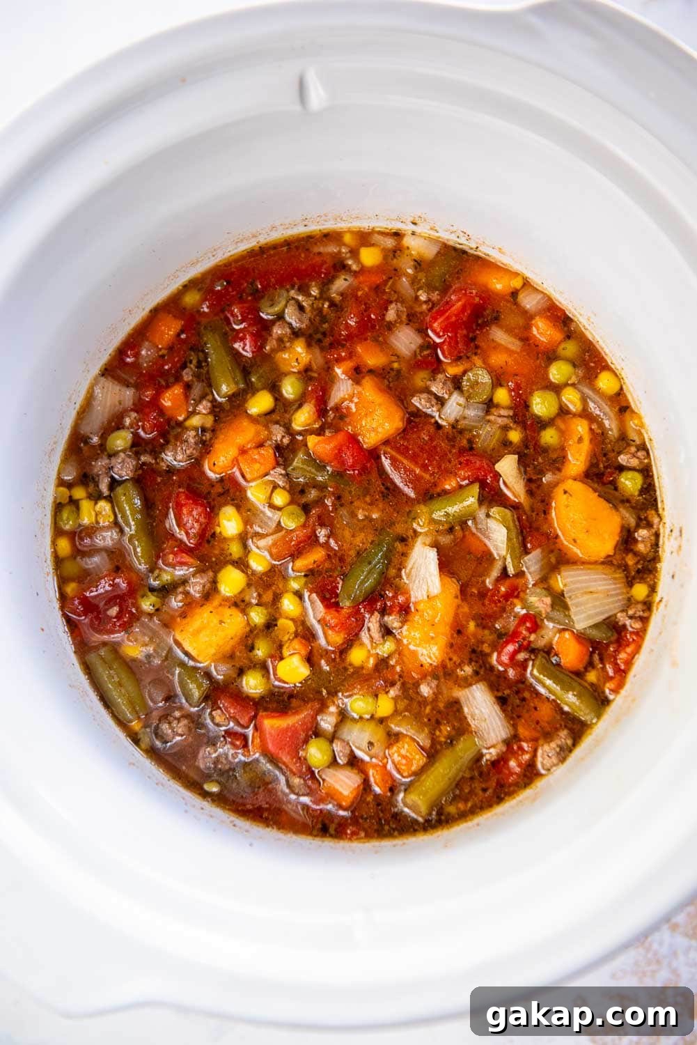 Ground beef, chopped shallot, mixed vegetables, and petite diced tomatoes cooking in slow cooker