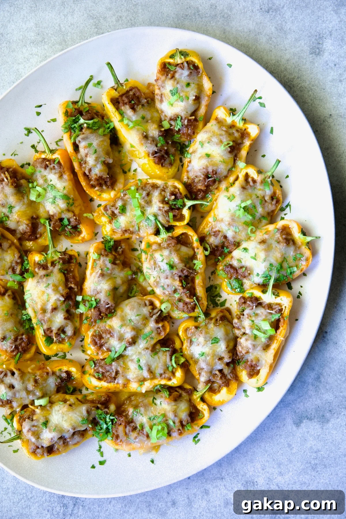 Mini Pepper Tacos: Flavor-Packed Taco-Stuffed Peppers 11 Taco-Stuffed Mini Peppers on white oval platter garnished with thinly sliced scallion and chopped cilantro.